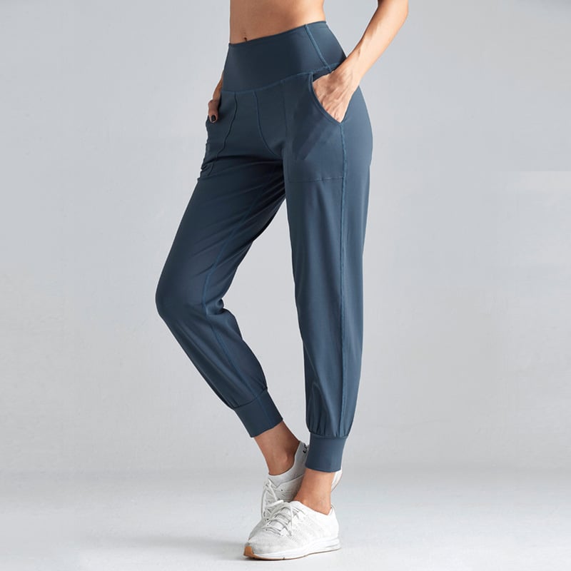 Donna in pantaloni sportivi blu, tasche laterali, vita alta, abbinati a scarpe da ginnastica bianche. Abbigliamento fitness comodo ed elegante.