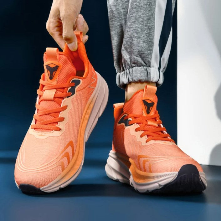 Scarpe da corsa arancioni con suola ammortizzata, design moderno e logo nero, indossate con pantaloni sportivi grigi. Calzature sportive uomo.