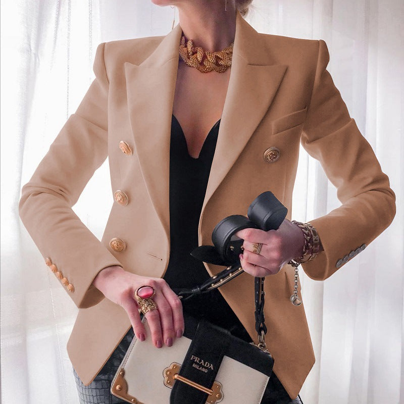 Donna elegante con blazer beige a doppiopetto, abito nero scollato, collana dorata, anelli vistosi e borsa Prada. Moda di lusso, stile sofisticato.