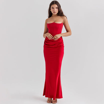 Donna in abito lungo rosso elegante, senza spalline, con drappeggio in vita, posa su sfondo neutro. Moda femminile, abbigliamento da sera.