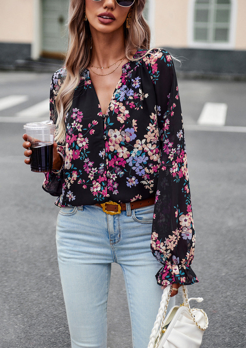 Donna con camicetta floreale nera, jeans chiari, occhiali da sole e borsa bianca, tiene una bevanda. Moda casual femminile, street style elegante.