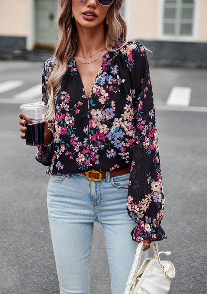 Donna con camicetta floreale nera, jeans chiari, occhiali da sole e borsa bianca, tiene una bevanda. Moda casual femminile, street style elegante.
