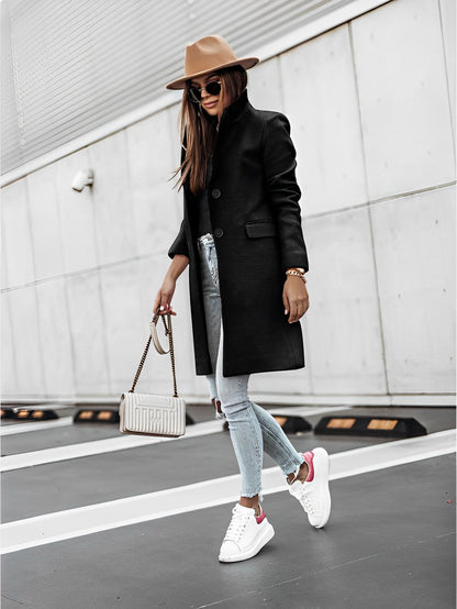 Donna alla moda con cappotto nero, jeans strappati, sneakers bianche e cappello marrone. Borsa a tracolla bianca. Look urbano chic.