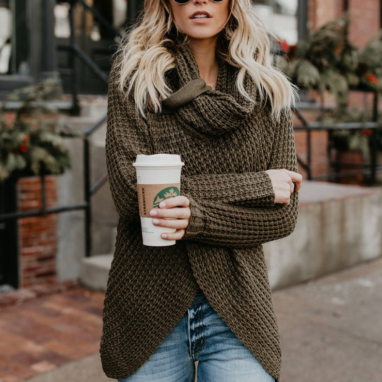 Donna con maglione a maglia verde oliva, occhiali da sole, tiene caffè Starbucks. Moda autunnale, look casual urbano. Sfondo urbano sfocato.