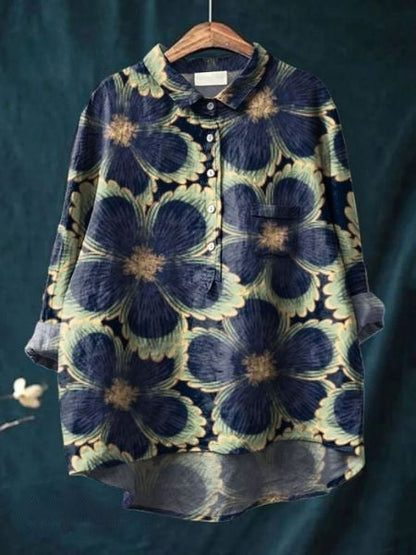 Camicia floreale oversize con motivo a fiori blu e verdi su sfondo scuro, appesa su gruccia di legno. Moda casual, abbigliamento donna.