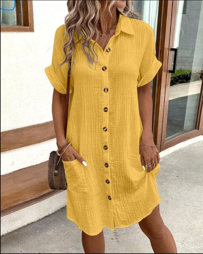 Donna con abito chemisier giallo, bottoni frontali, tasche laterali, capelli ondulati, borsa a tracolla marrone, stile casual estivo.
