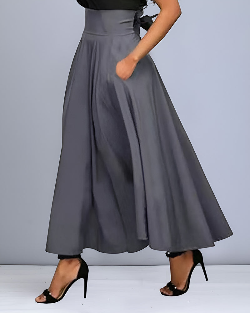 Donna in gonna lunga grigia a vita alta, con tasche, abbinata a sandali neri con tacco. Elegante abbigliamento femminile per occasioni formali.