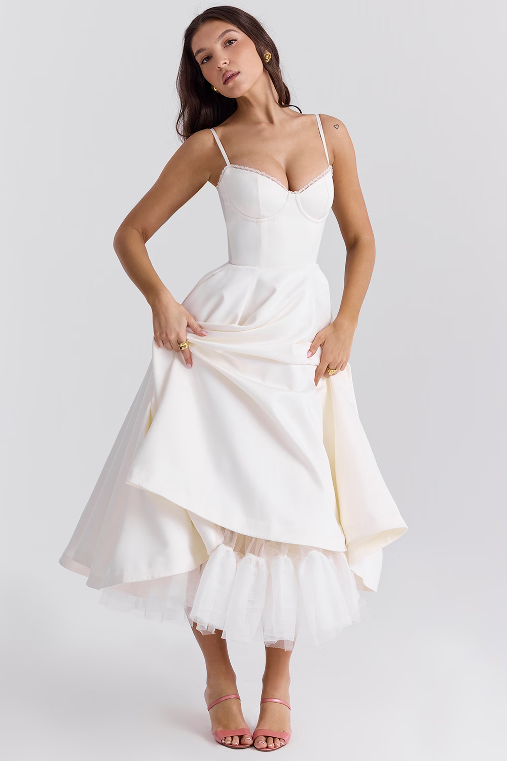 Donna in abito da sposa bianco elegante, con corpetto aderente e gonna ampia, posa su sfondo neutro. Moda nuziale, abbigliamento cerimonia.
