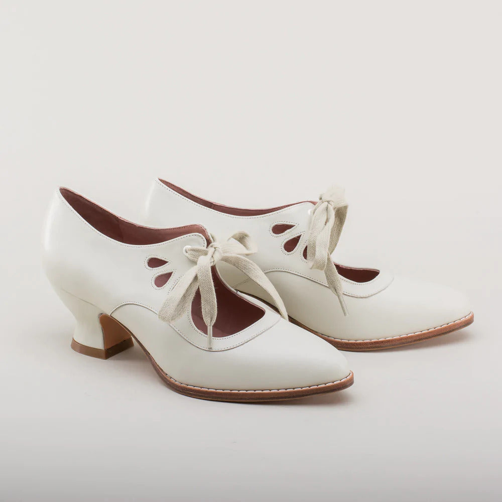 Scarpe vintage bianche con tacco medio, lacci in tessuto e dettagli traforati. Eleganti calzature retrò per donna, stile anni '20.
