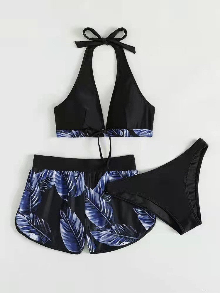Costume da bagno donna nero con foglie blu, composto da top allacciato al collo, slip e pantaloncini coordinati. Design estivo elegante e moderno.
