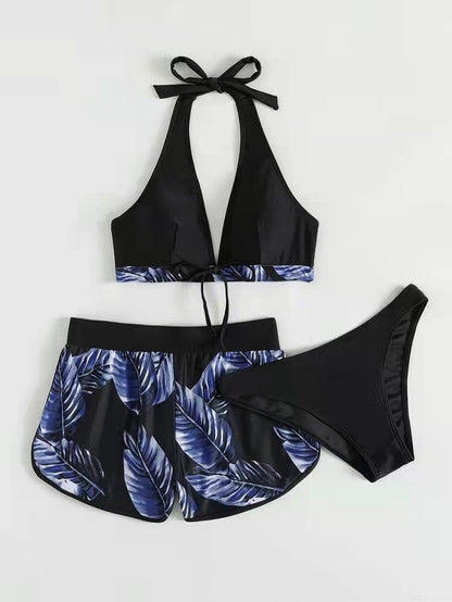 Costume da bagno donna nero con foglie blu, composto da top allacciato al collo, slip e pantaloncini coordinati. Design estivo elegante e moderno.