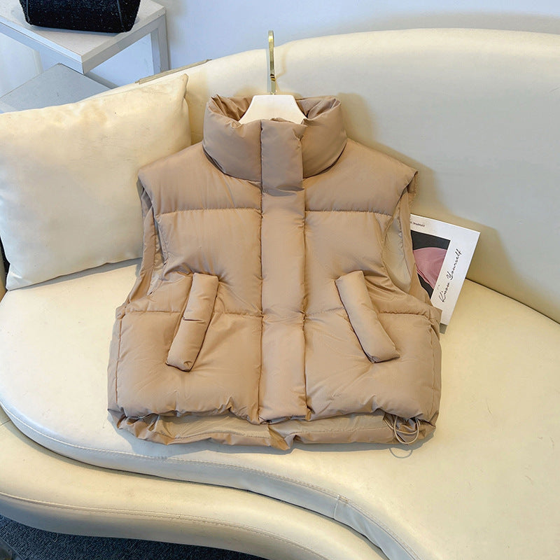 Gilet imbottito beige su divano bianco, design senza maniche, tasche frontali, ideale per moda autunnale e invernale.