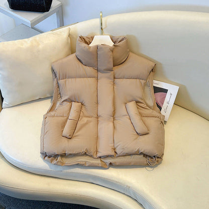 Gilet imbottito beige su divano bianco, design senza maniche, tasche frontali, ideale per moda autunnale e invernale.