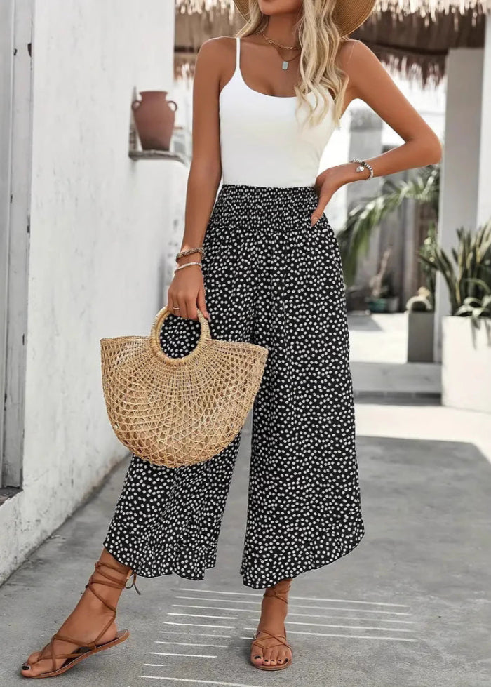 Donna con top bianco e pantaloni a pois neri, borsa di paglia, sandali marroni. Moda estiva casual, outfit elegante per passeggiate in città.