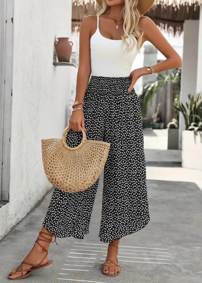 Donna con top bianco e pantaloni a pois neri, borsa di paglia, sandali marroni. Moda estiva casual, outfit elegante per passeggiate in città.