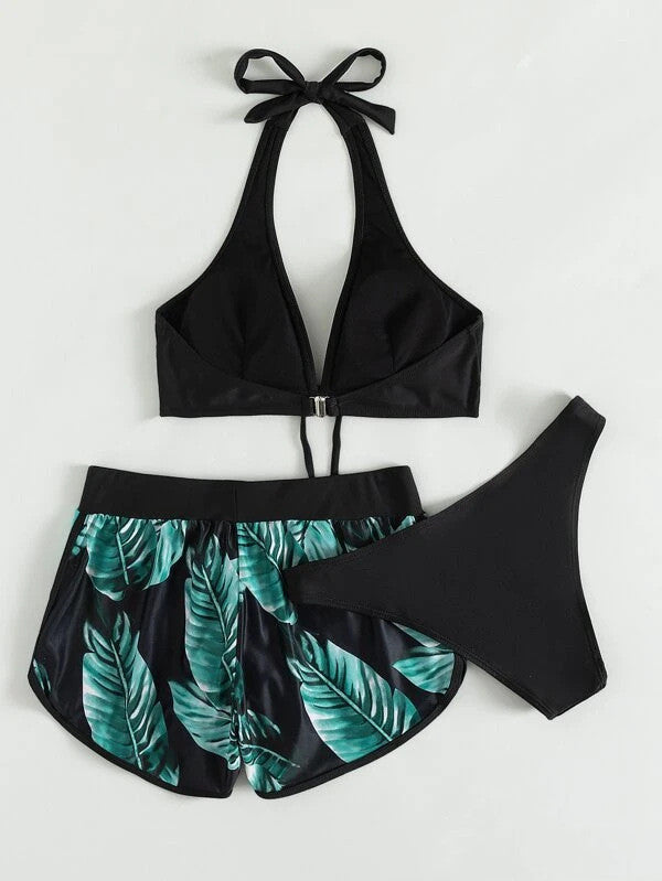 Costume da bagno donna nero con top a triangolo, slip e pantaloncini con stampa foglie tropicali verdi. Moda mare estiva, abbigliamento da spiaggia.