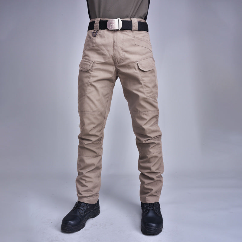 Pantaloni cargo beige da uomo con tasche multiple, cintura nera e fibbia argentata, abbinati a stivali neri. Abbigliamento casual e funzionale.