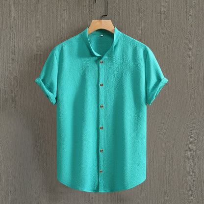 Camicia verde acqua a maniche corte, tessuto leggero, colletto alla coreana, bottoni in legno, appesa su gruccia. Moda estiva casual uomo.