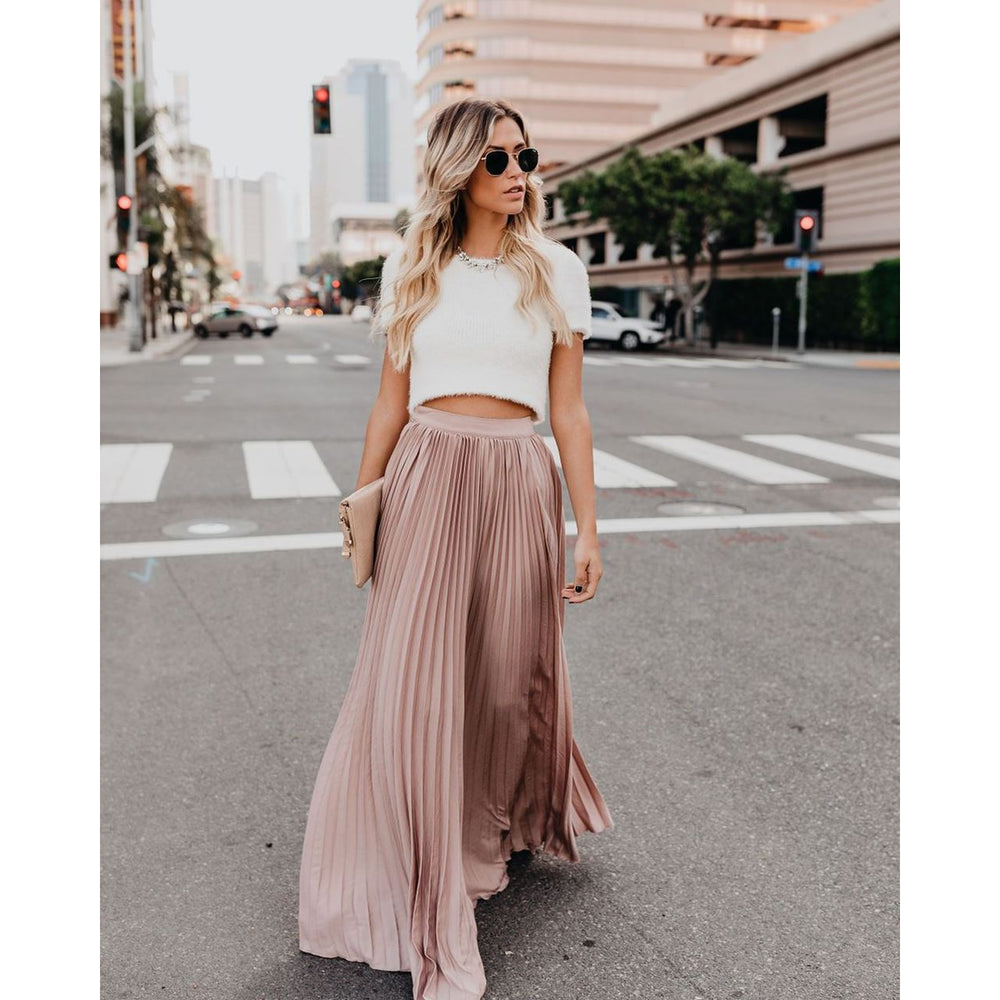 Donna alla moda con occhiali da sole, top bianco e gonna lunga plissettata rosa, cammina in città. Stile urbano, moda estiva, look elegante.