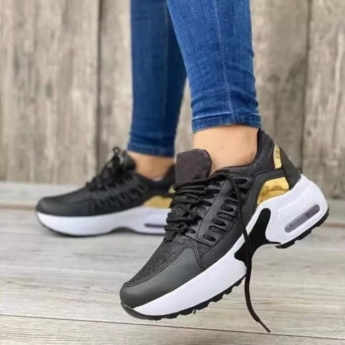 Scarpe da ginnastica nere e oro con suola bianca, indossate da una persona in jeans. Design moderno, ideali per sport e moda casual.