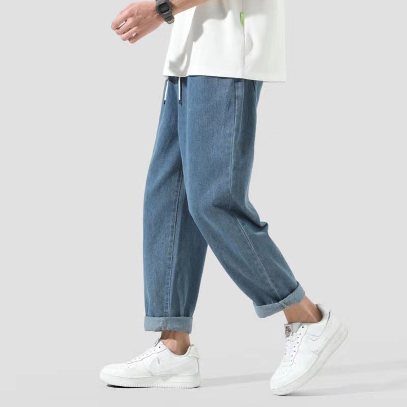 Jeans larghi da uomo, stile casual, abbinati a scarpe da ginnastica bianche e maglietta bianca, moda streetwear, sfondo grigio chiaro.