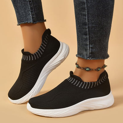 Scarpe da ginnastica nere senza lacci con suola bianca, indossate con jeans aderenti e cavigliera decorativa. Moda casual, comfort, stile urbano.