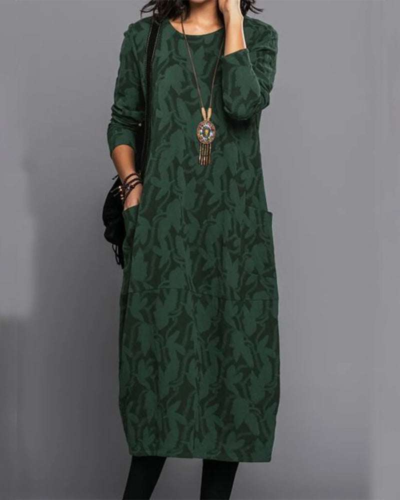 Abito lungo verde scuro con motivo floreale, maniche lunghe, tasche laterali e collana pendente. Moda donna autunno, stile casual elegante.