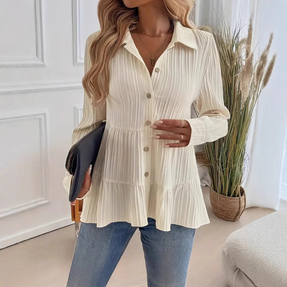 Donna con camicia bianca a coste, jeans blu, borsa nera, in un interno moderno con piante decorative. Moda casual elegante, stile autunnale.