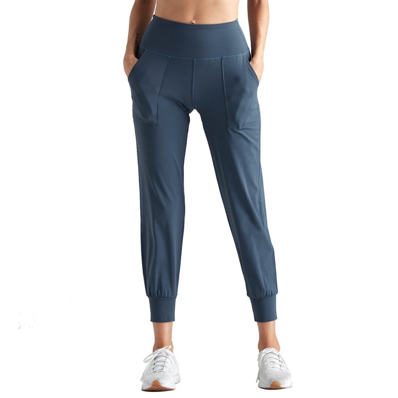 Pantaloni sportivi donna blu, vita alta, tasche laterali, tessuto elasticizzato, ideali per yoga e fitness. Scarpe da ginnastica bianche incluse.
