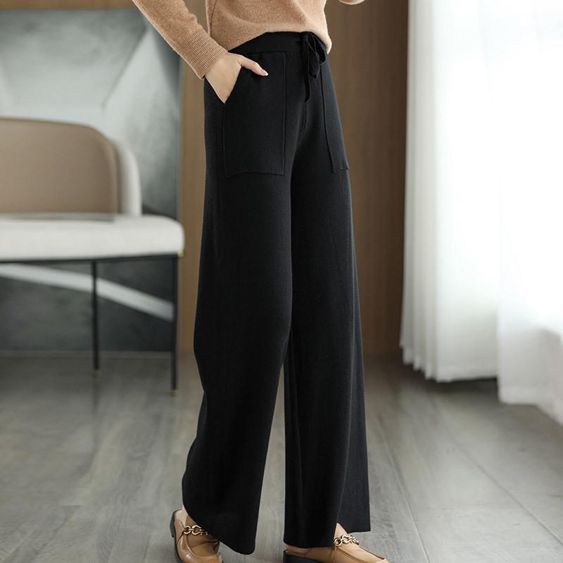 Pantaloni neri larghi da donna, eleganti e comodi, con tasche frontali, indossati con mocassini marroni su pavimento in legno chiaro.