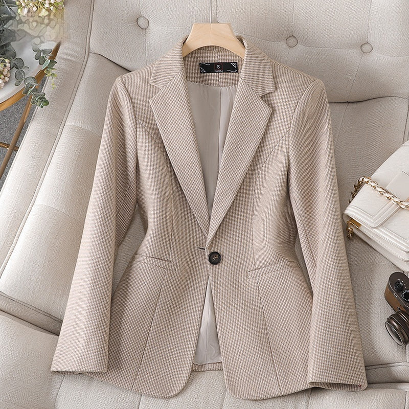 Giacca elegante beige da donna su poltrona, tessuto a trama fine, abbinata a borsa bianca e fotocamera vintage. Moda femminile, abbigliamento chic.