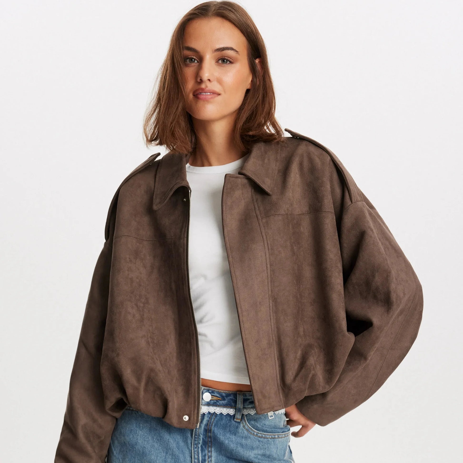 Donna con giacca oversize marrone in pelle scamosciata, maglietta bianca e jeans. Moda autunnale casual, stile contemporaneo.