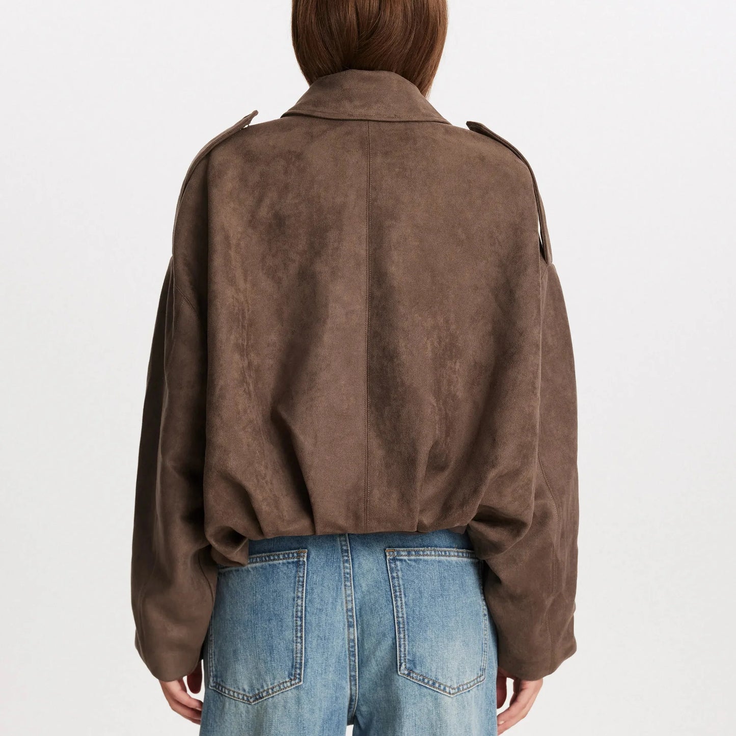 Donna di spalle con giacca marrone scamosciata e jeans blu. Moda autunnale, abbigliamento casual, stile urbano.