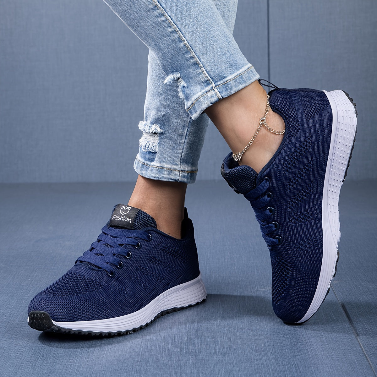 Scarpe da ginnastica blu scuro su sfondo blu, indossate con jeans strappati. Design moderno, suola bianca, perfette per moda casual e sportiva.