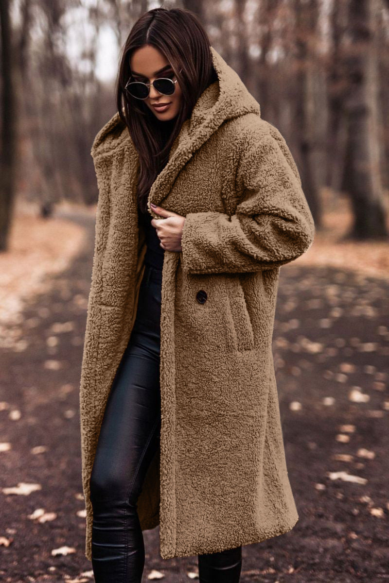 Donna con cappotto teddy beige, occhiali da sole neri, pantaloni in pelle nera, passeggia in un parco autunnale. Moda autunno inverno, stile casual chic.