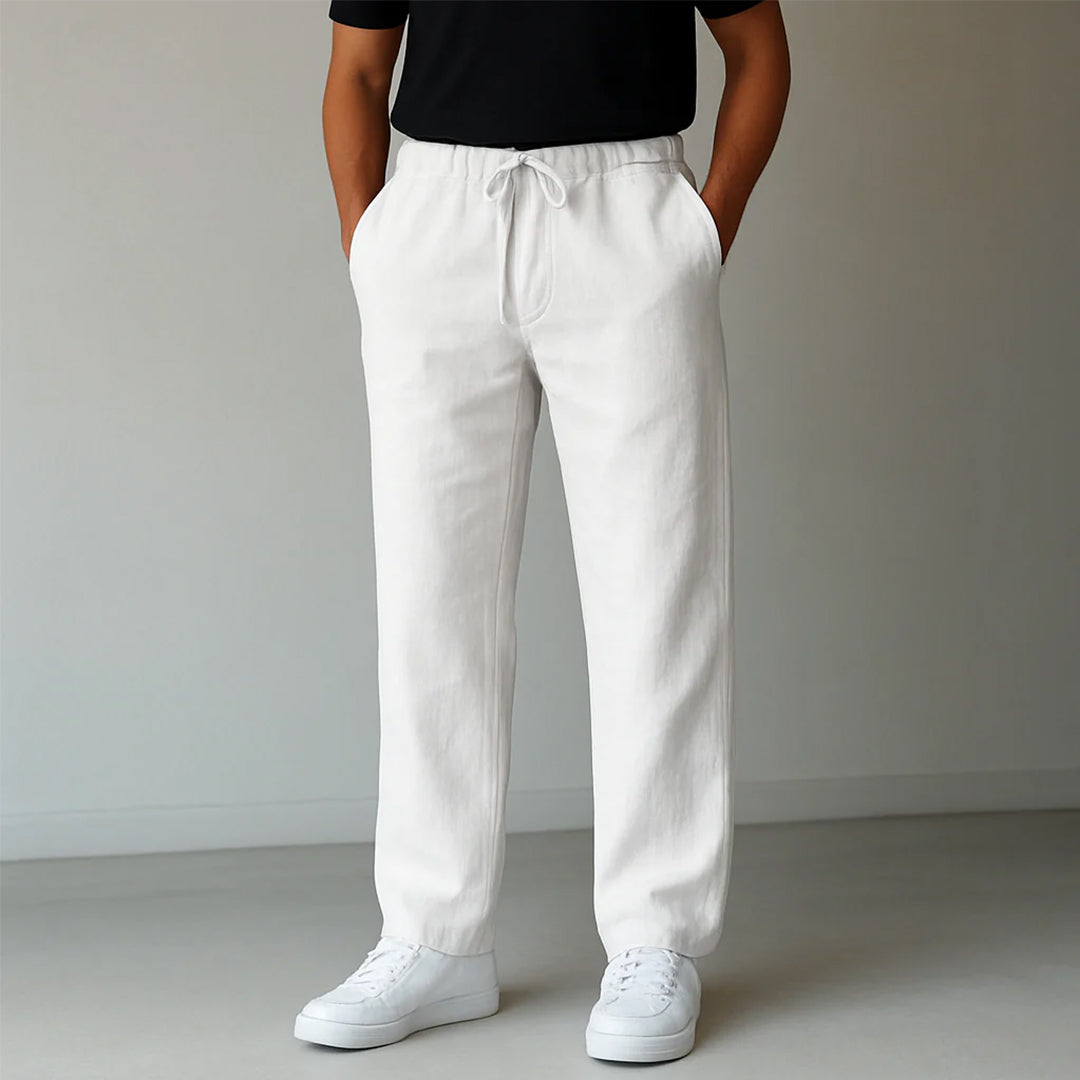 Pantaloni bianchi da uomo in lino, stile casual, con coulisse in vita, abbinati a scarpe da ginnastica bianche e maglietta nera.