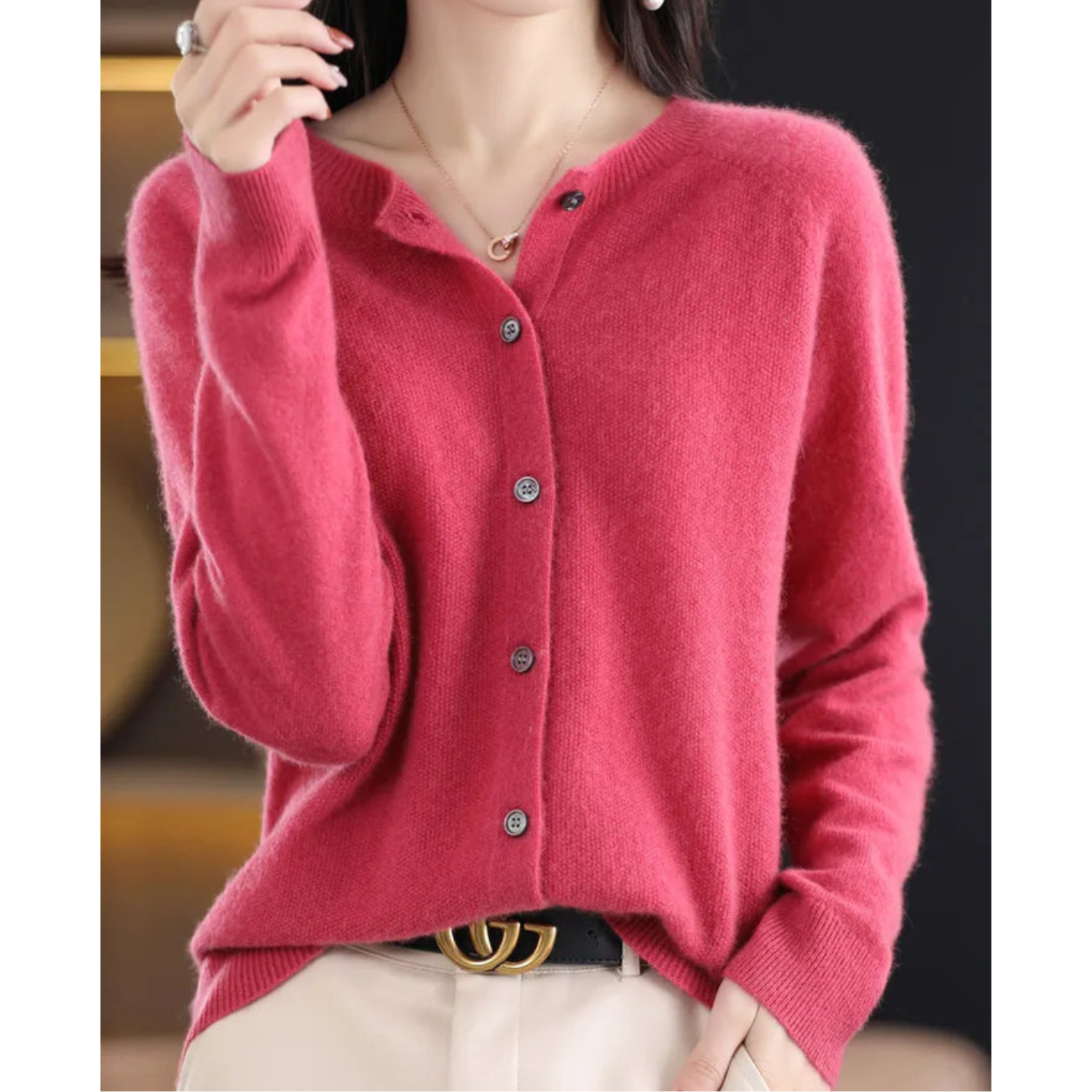 Donna con cardigan rosa in cashmere, bottoni grigi, indossa pantaloni chiari e cintura nera con fibbia dorata. Moda autunnale elegante.
