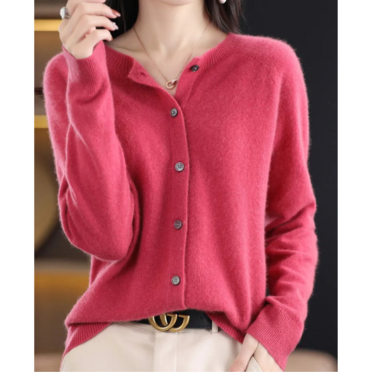 Donna con cardigan rosa in cashmere, bottoni grigi, indossa pantaloni chiari e cintura nera con fibbia dorata. Moda autunnale elegante.