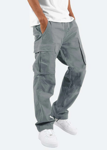 Pantaloni cargo grigi da uomo, tasche multiple, stile casual, abbinati a scarpe da ginnastica bianche e maglietta bianca. Moda urbana maschile.