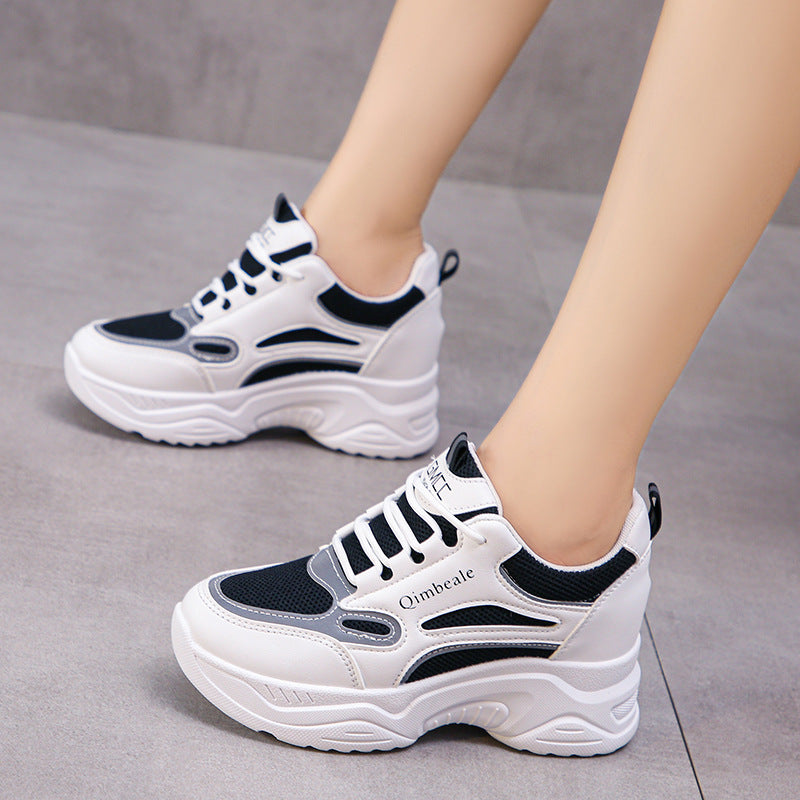 Scarpe da ginnastica bianche e nere su pavimento grigio, design moderno con suola spessa. Scarpe sportive alla moda per donna, comfort e stile.