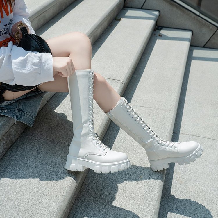 Stivali bianchi alti con lacci su gradini di cemento, indossati da una persona con abbigliamento casual. Scarpe moda autunno, stile urbano.