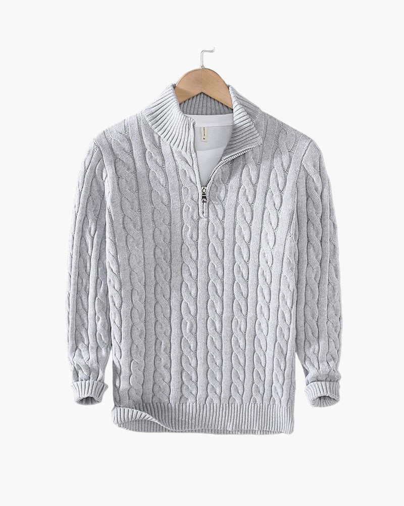 Maglione grigio a trecce con zip, collo alto, in lana, appeso su gruccia. Design elegante e caldo, ideale per moda invernale e autunnale.
