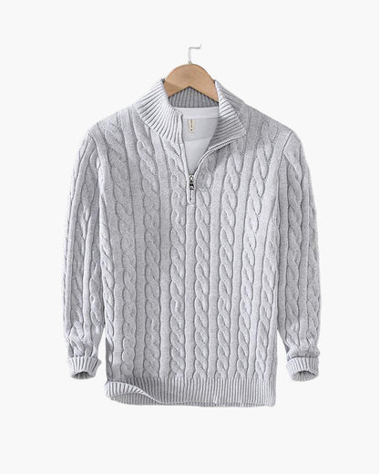 Maglione grigio a trecce con zip, collo alto, in lana, appeso su gruccia. Design elegante e caldo, ideale per moda invernale e autunnale.