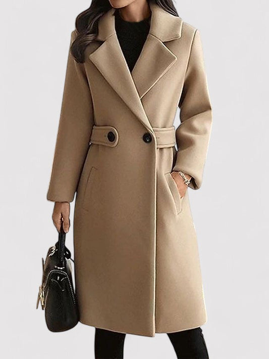 Cappotto beige elegante da donna, lungo, con bottoni neri e cintura, abbinato a borsa nera. Moda autunnale, stile classico e sofisticato.