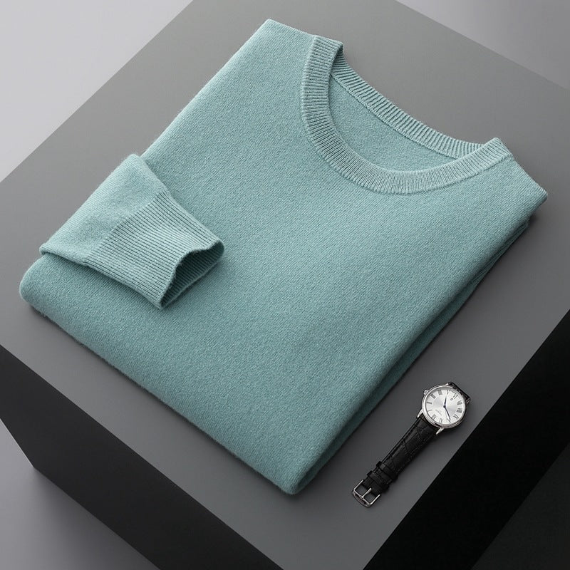 Maglione verde menta piegato su tavolo grigio, accanto a orologio da polso con cinturino in pelle nera. Moda elegante, abbigliamento invernale.