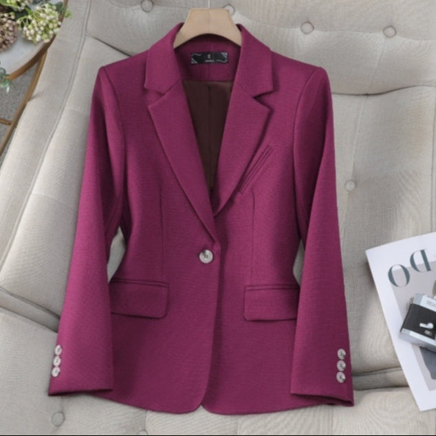 Giacca elegante da donna color magenta su divano beige, con bottoni decorativi e tasche, ideale per moda autunnale e abbigliamento formale.