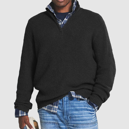 Maglione nero a collo alto con zip, indossato sopra una camicia a quadri blu e jeans. Look casual e moderno per uomo.