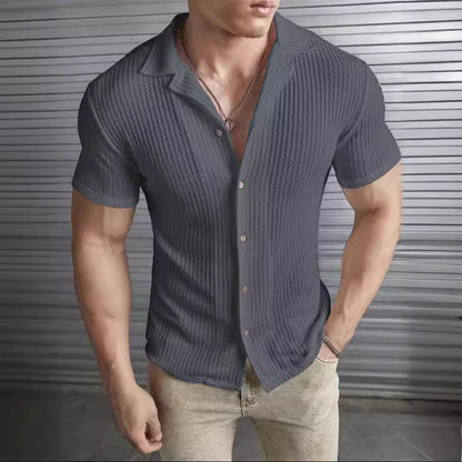 Uomo in camicia a righe blu scuro, maniche corte, davanti a una parete metallica. Moda maschile, abbigliamento casual elegante.