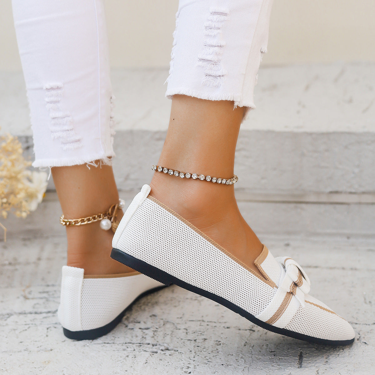 Scarpe da donna bianche eleganti con fiocco, indossate con jeans strappati bianchi. Accessori: cavigliere dorate e argentate. Moda estiva casual.