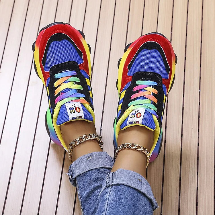 Scarpe da ginnastica multicolore su pavimento in legno, lacci arcobaleno, jeans. Sneakers moda, stile casual, calzature trendy.